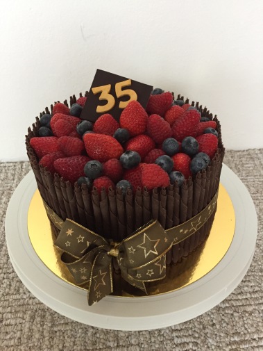Čokoládový dort s malinami, zdobený čokoládovými tyčinkami, stuhou a lesním ovocem